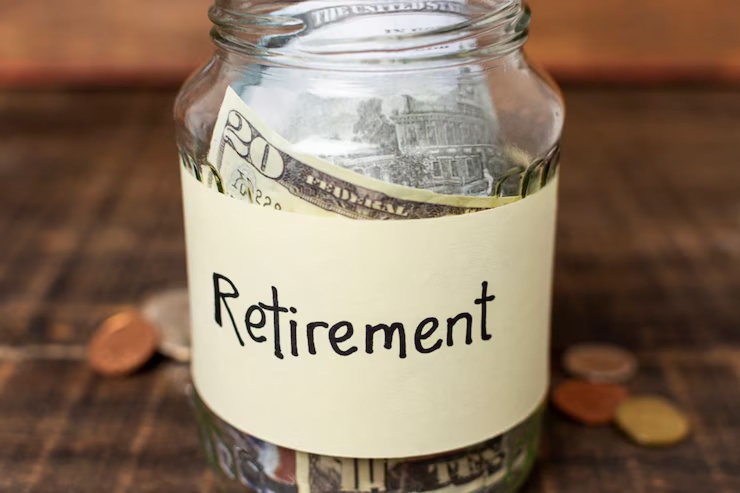 Glass jar labeled "Retirement" filled with U.S. dollar bills and coins, placed on a wooden surface, representing long-term savings and the principles of the FIRE (Financial Independence, Retire Early) movement.