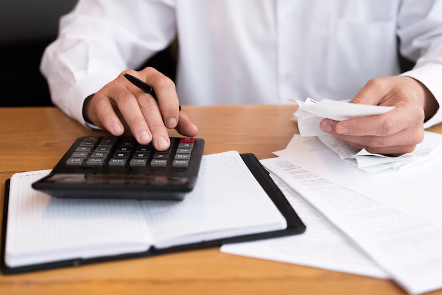 A person in a white shirt uses a calculator and reviews receipts at a desk covered with financial documents, illustrating the careful budgeting often influenced by interest rate changes set by the Fed (The Federal Reserve).