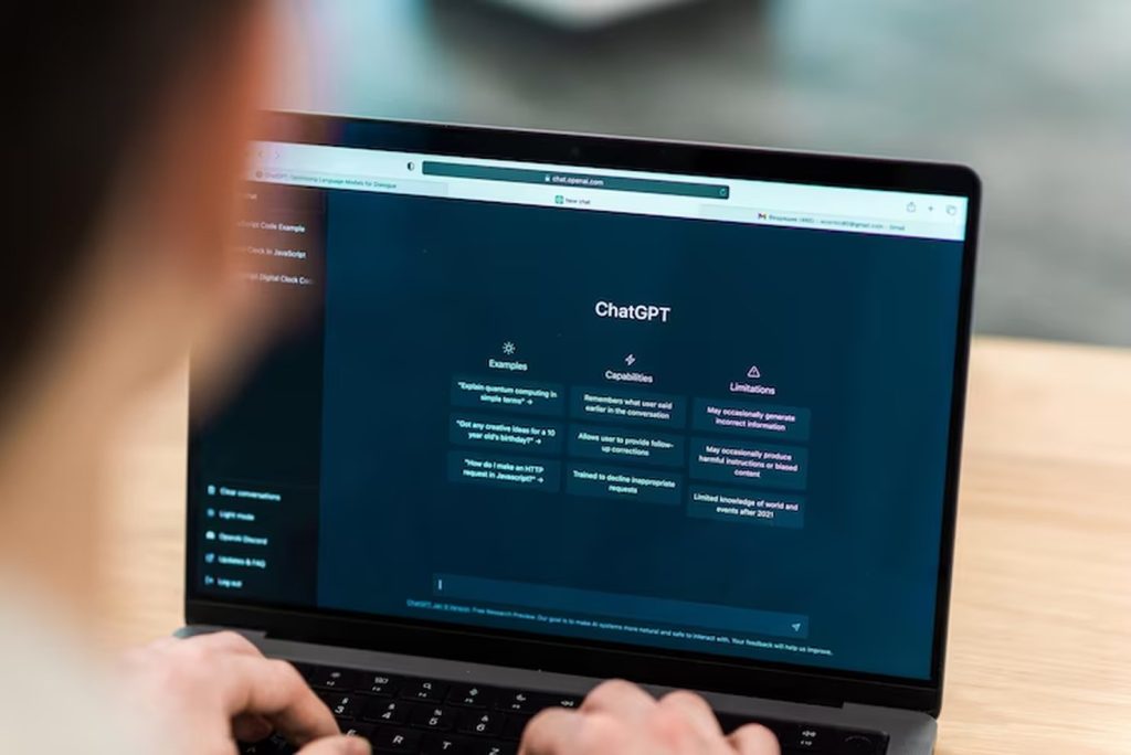 A person uses a laptop displaying the ChatGPT interface, highlighting example prompts, capabilities, and limitations — a practical setting for learning how to use ChatGPT effectively in real-world scenarios.
