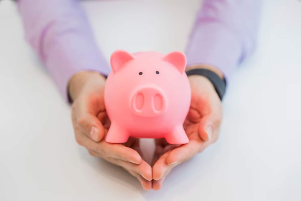 Person wearing a light purple shirt gently holding a pink piggy bank, symbolizing protection and financial planning through savings accounts.